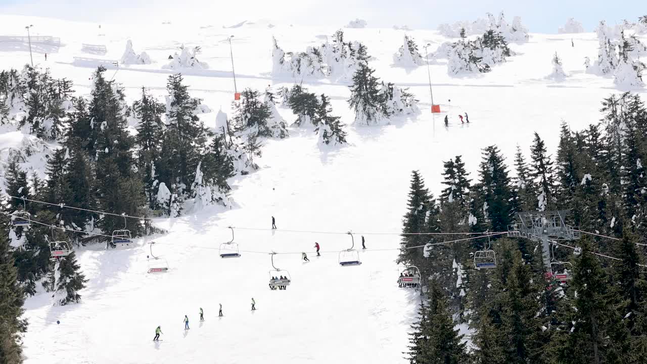 在阳光明媚的冬日，可在索道上升降的升降机及在斜坡上滑雪的滑雪者视频素材