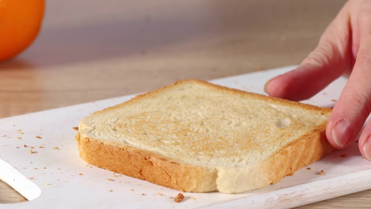 女人的手在一片烤面包上涂上橙色的杏子酱。家庭烹饪早餐视频素材