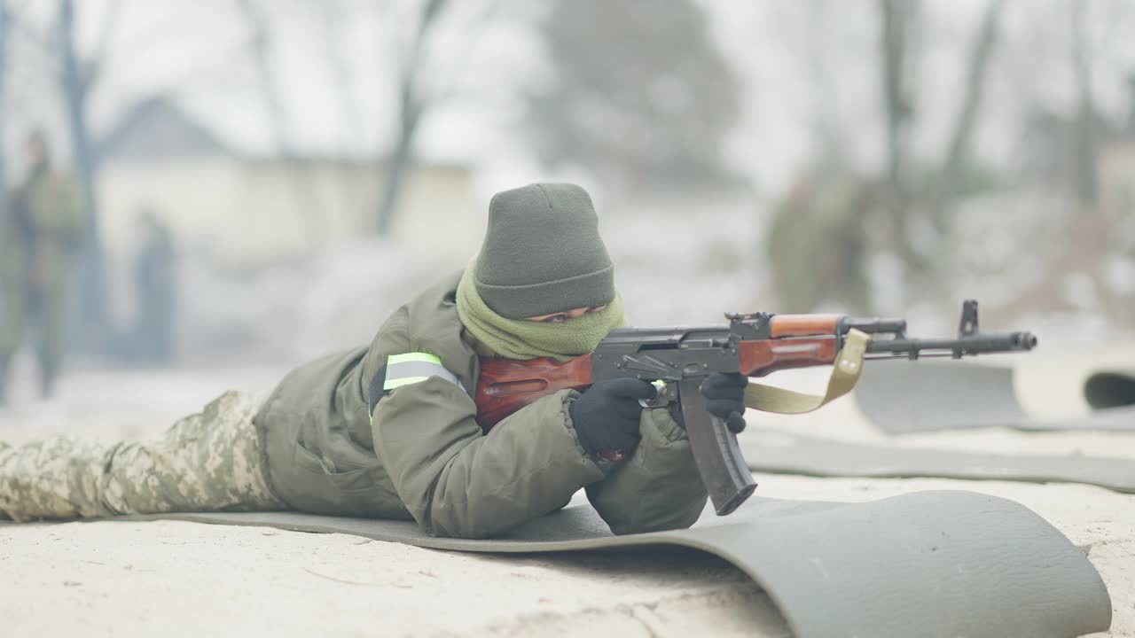 严肃自信的女兵躺在多边形上，用步枪慢动作射击。职业白人女军人在户外训练的肖像。视频素材