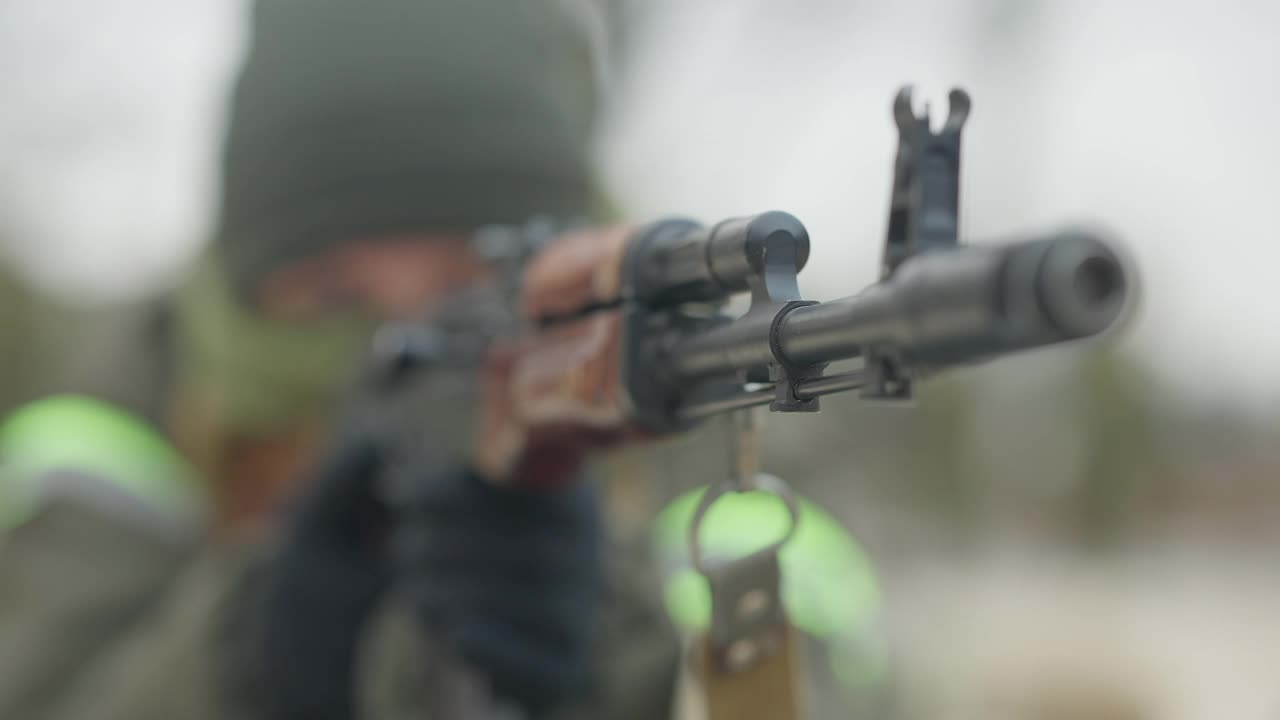 枪点的特写镜头，模糊的白人士兵瞄准背景。军队武器与蒙面女军人训练多边形户外的特写。视频素材