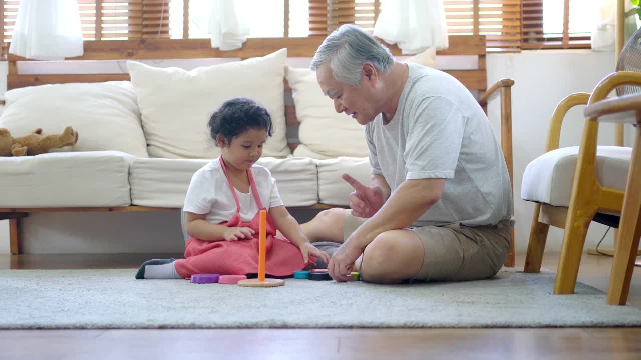 快乐的爷爷和小孙女在家里的客厅里玩视频素材