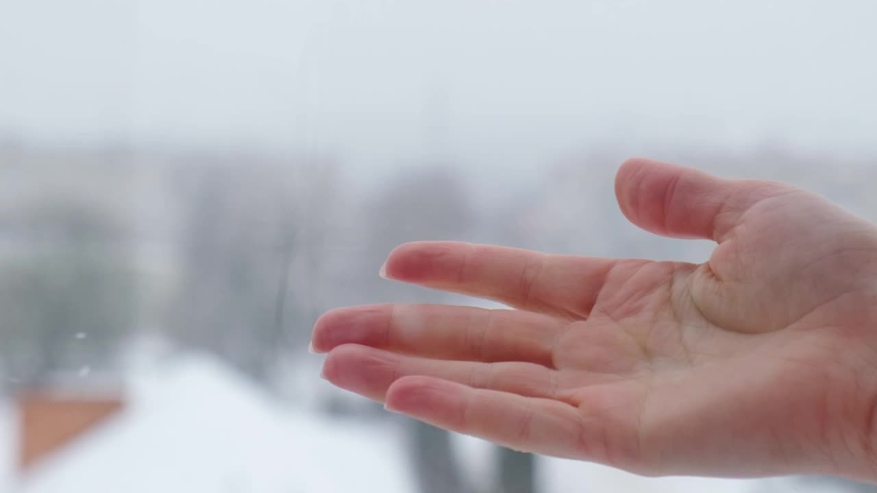 雪落到女人手里的慢动作。白雪覆盖的城市，雪花飞舞的慢镜头。散焦。有选择性的重点。模糊的冬季背景寒冷的天气视频素材