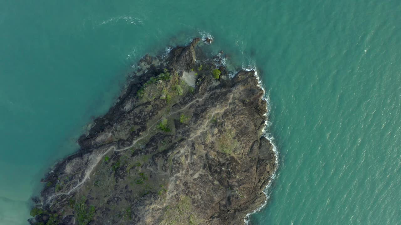 空中盘旋在一个小岩石岛上升出海洋，与锯齿状的岩石，绿色的计划，旋转的海水，和近黄昏温暖的阳光-约克角，澳大利亚视频素材