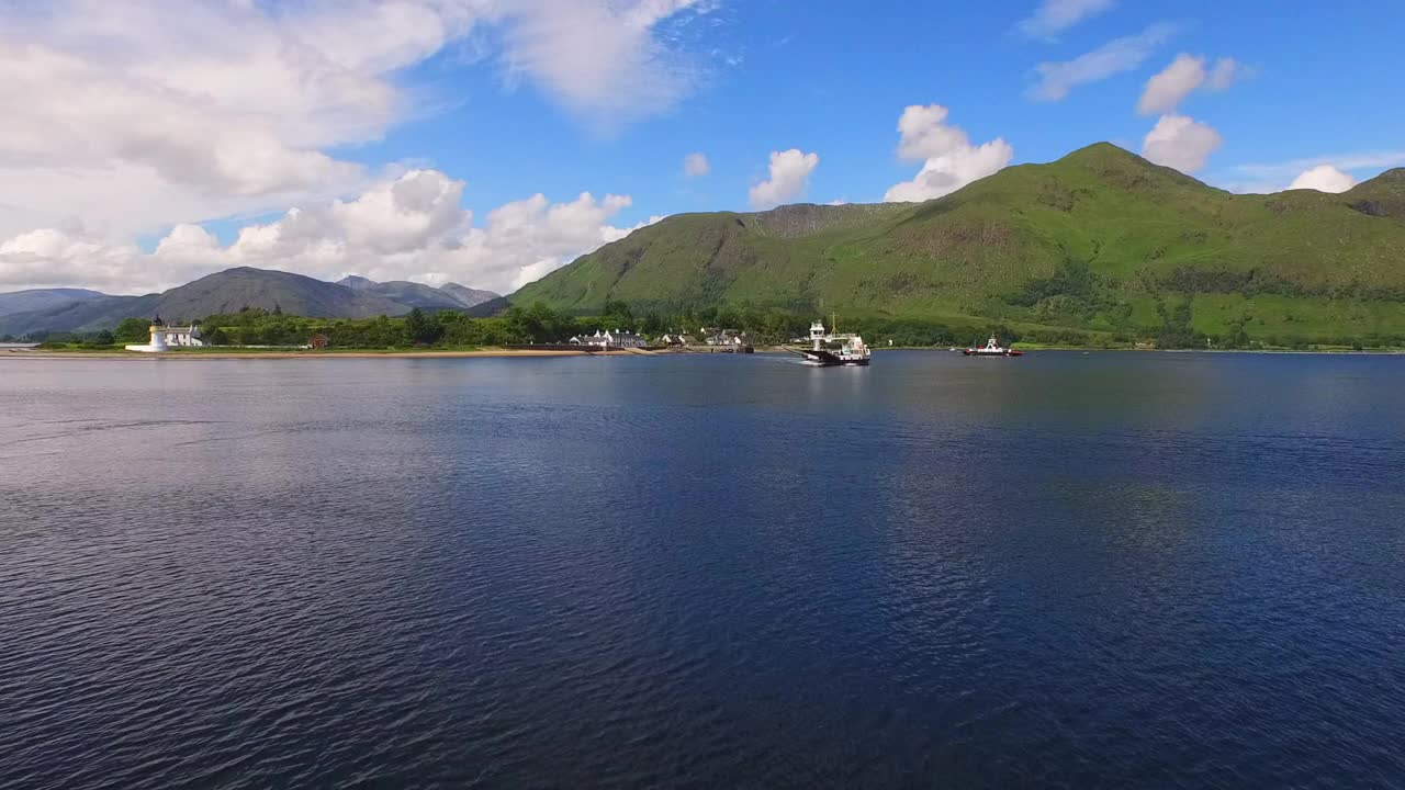 空中接近一艘渡轮，因为它离开了一个偏远的山区海岸线，村庄建筑，深蓝色的海水，明亮的蓝天-提里岛，英国视频素材