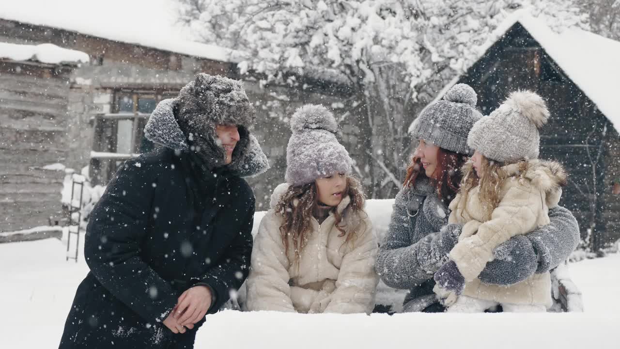 冬季家庭乐趣。快乐的四口之家享受着雪花，在户外玩耍，在下雪的冬天一起度过时光。慢动作视频素材