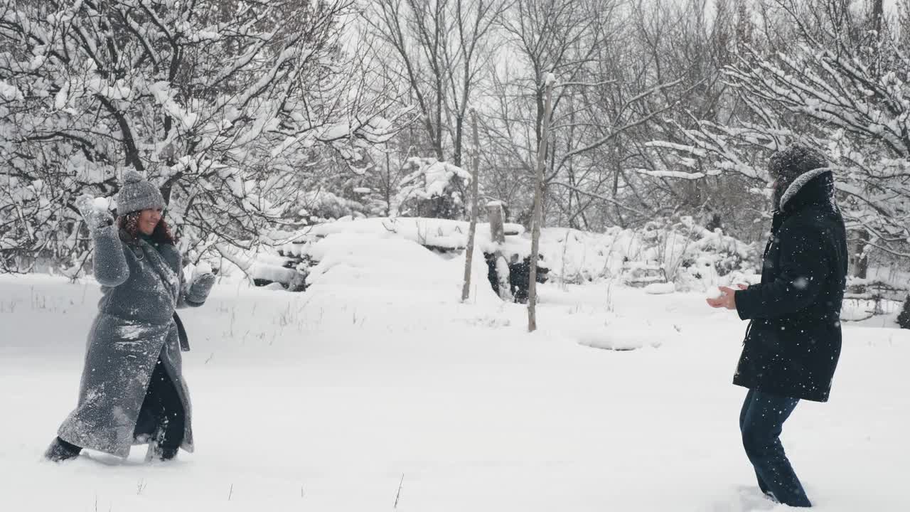 下雪的冬天的乐趣。扔雪球。幸福的一对，女人和男人在玩雪球，在户外玩，在下雪的冬天一起度过时光。慢动作视频素材