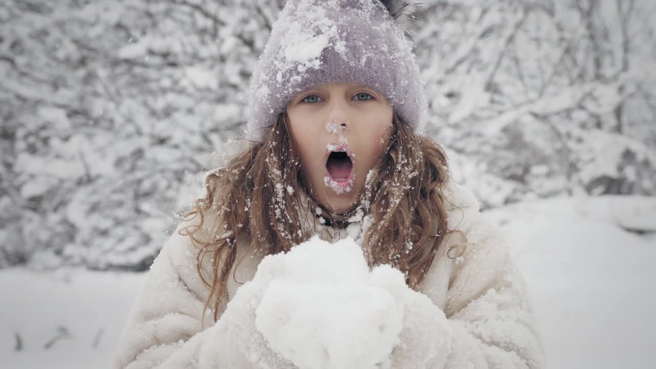 下雪的冬天的乐趣。吹雪。快乐的，可爱的，漂亮的，小女孩，穿着暖和的冬天的衣服，正在吹雪从手中的相机，在户外，在下雪的公园或森林视频素材