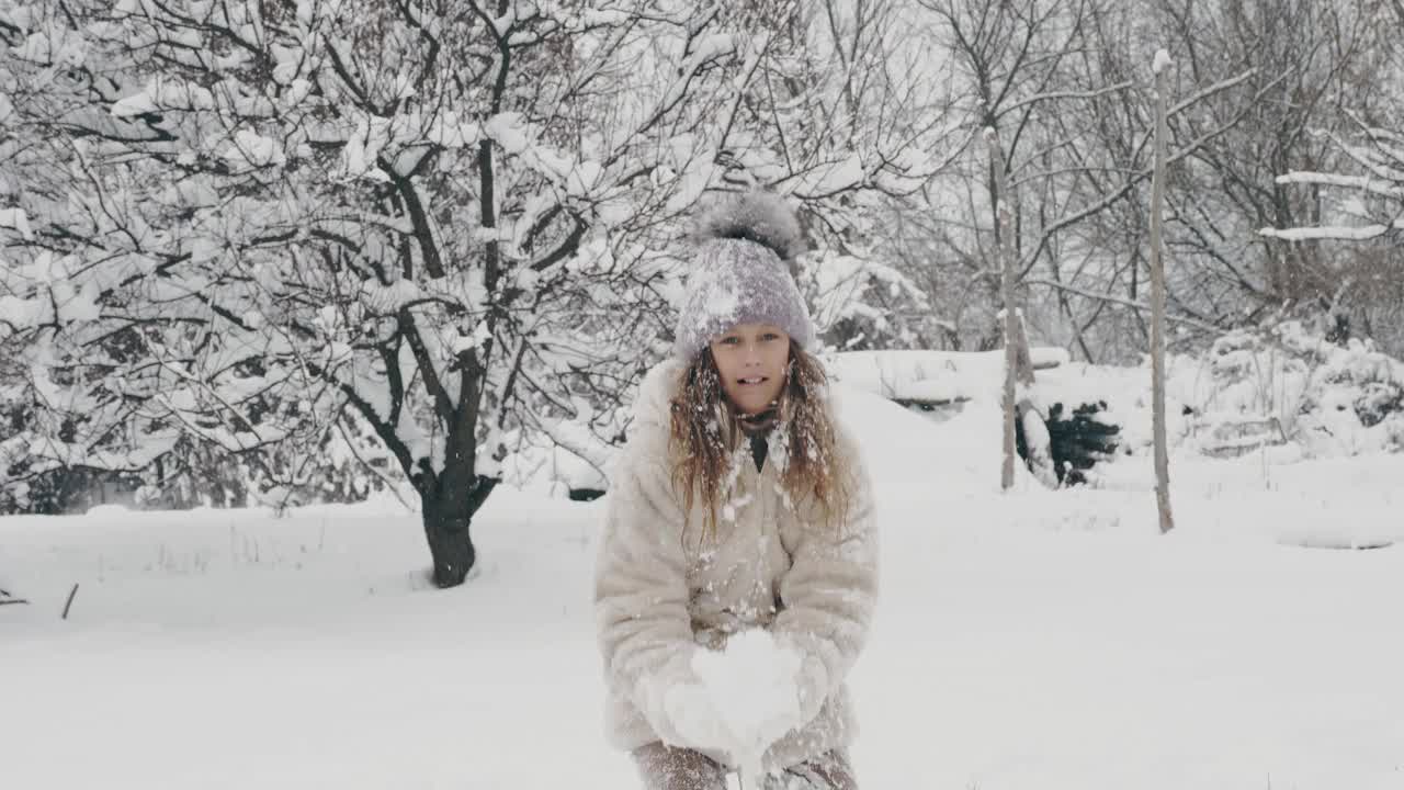 下雪的冬天的乐趣。快乐，可爱，漂亮的女孩，穿着暖和的冬天的衣服，正在把雪扔在自己身上，在下雪的时候，在户外玩，在下雪的日子，在公园或森林视频素材