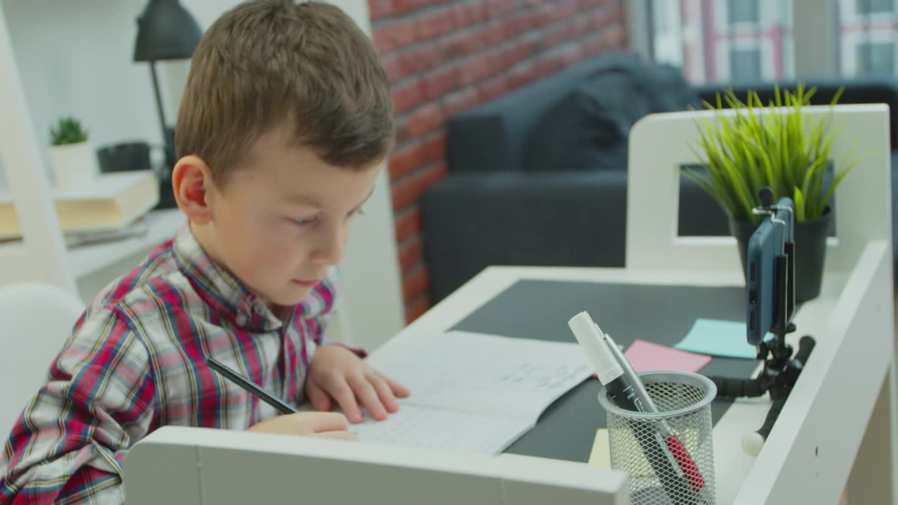 学生，在家远程学习。专注的小男孩使用智能手机应用程序，在视频课上学习。视频素材