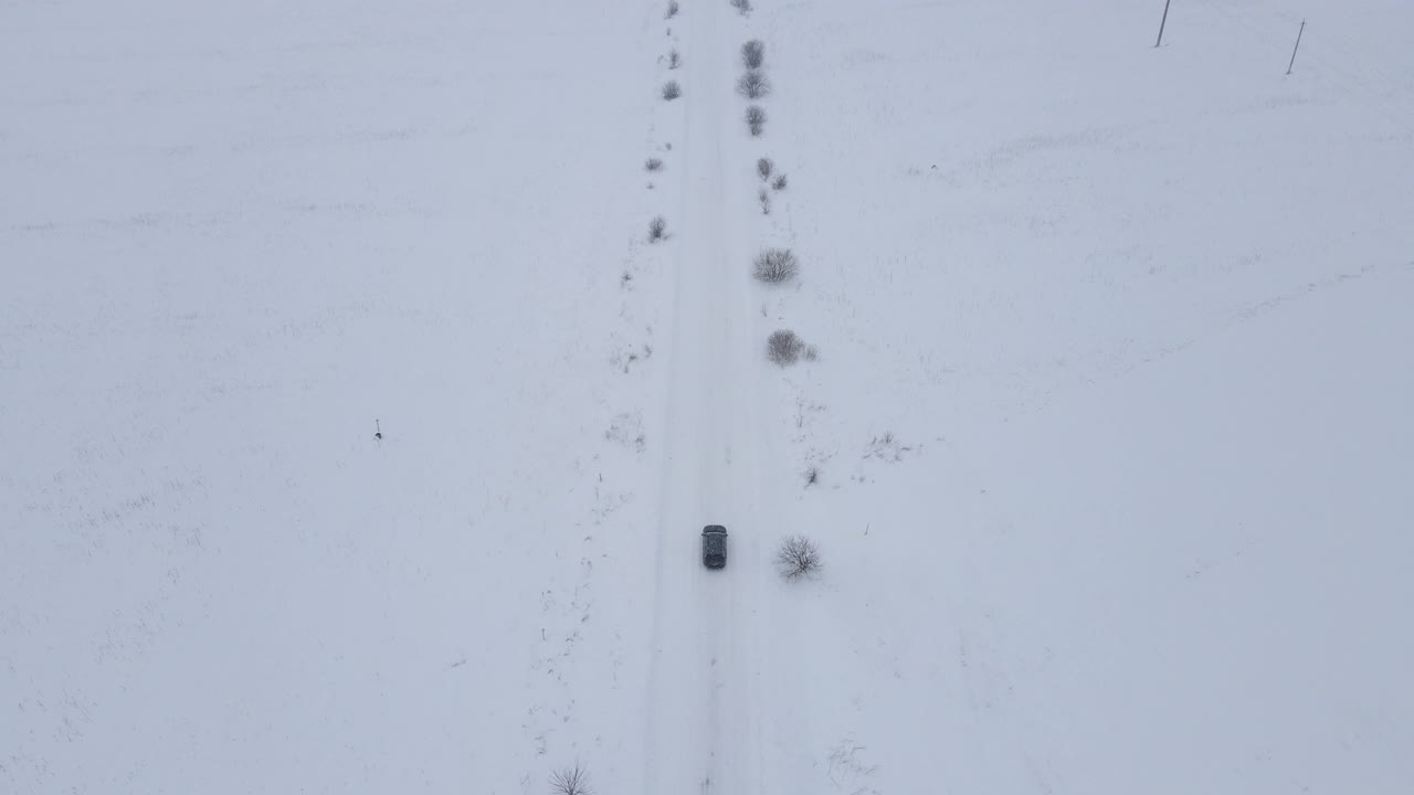 鸟瞰图汽车行驶在滑雪覆盖的道路上，当暴风雪覆盖着一层厚厚的积雪时，汽车在路上行驶视频素材