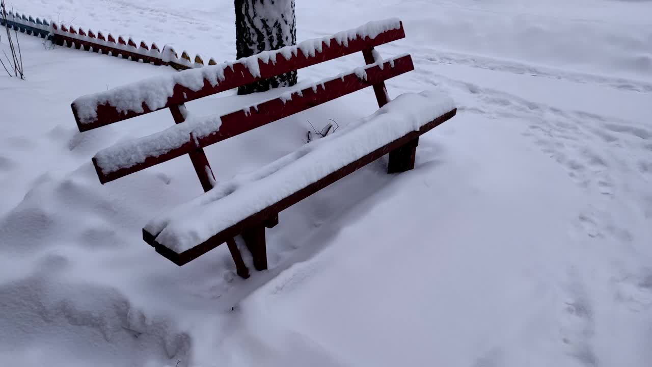 大雪过后，公园里的两张木凳被大雪完全覆盖。寒冷的冬日里下雪了，两条空长凳上覆盖着积雪。视频素材