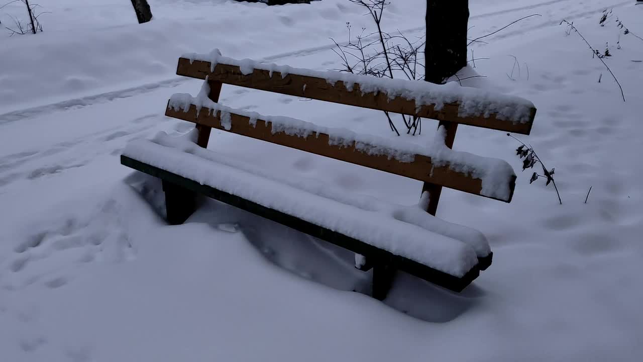 一场大雪过后，公园里的木凳完全被雪覆盖了。寒冷的冬日里下雪了，空荡荡的长凳上盖满了雪。视频素材