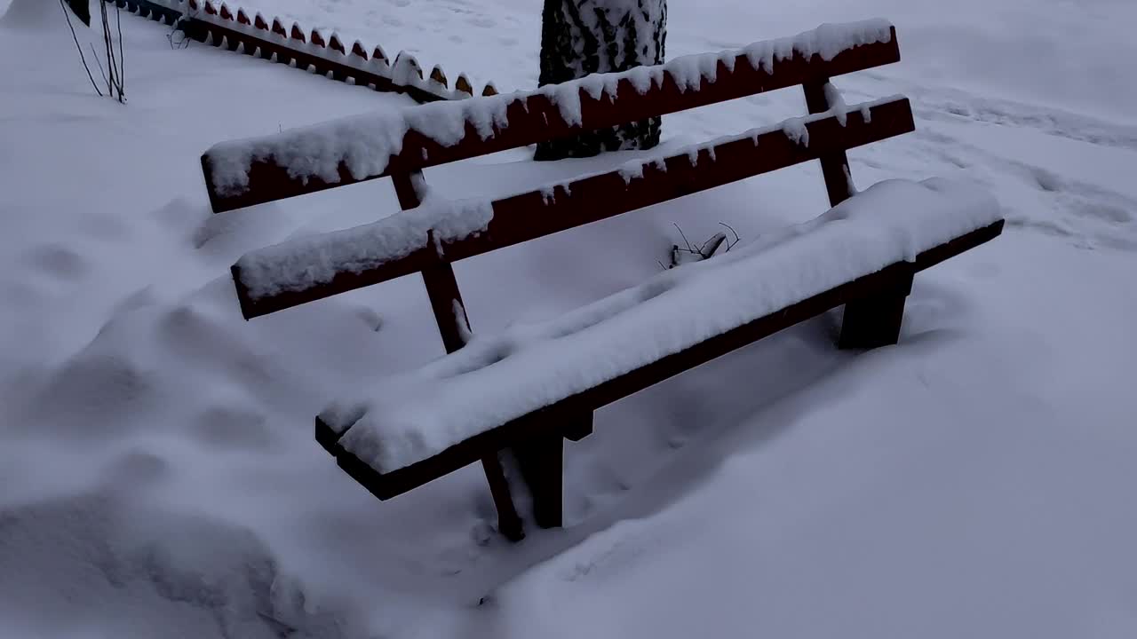 一场大雪过后，公园里的木凳完全被雪覆盖了。寒冷的冬日里下雪了，空荡荡的长凳上盖满了雪。视频素材