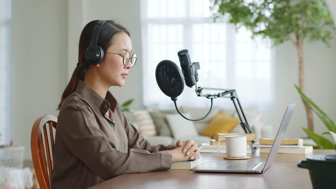 一名亚洲女子用麦克风在笔记本电脑上录制播客，同时在家进行在线直播视频素材