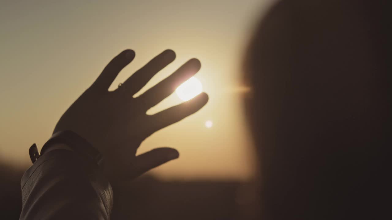 日落时，一个女人透过手指看太阳。手的特写镜头。视频素材