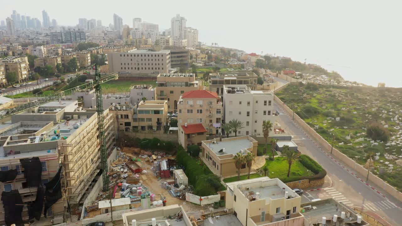 空中拍摄的街道在墓地和建筑物在日落，无人机上升在沿海城市的建筑工地海上-雅法，以色列视频素材