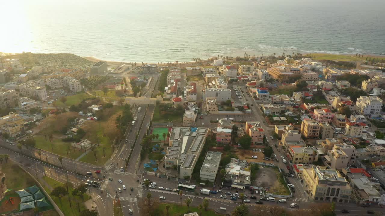 航拍在街道上的车辆在沿海城市的建筑物中，无人机下降向海岸线在日落-雅法，以色列视频素材