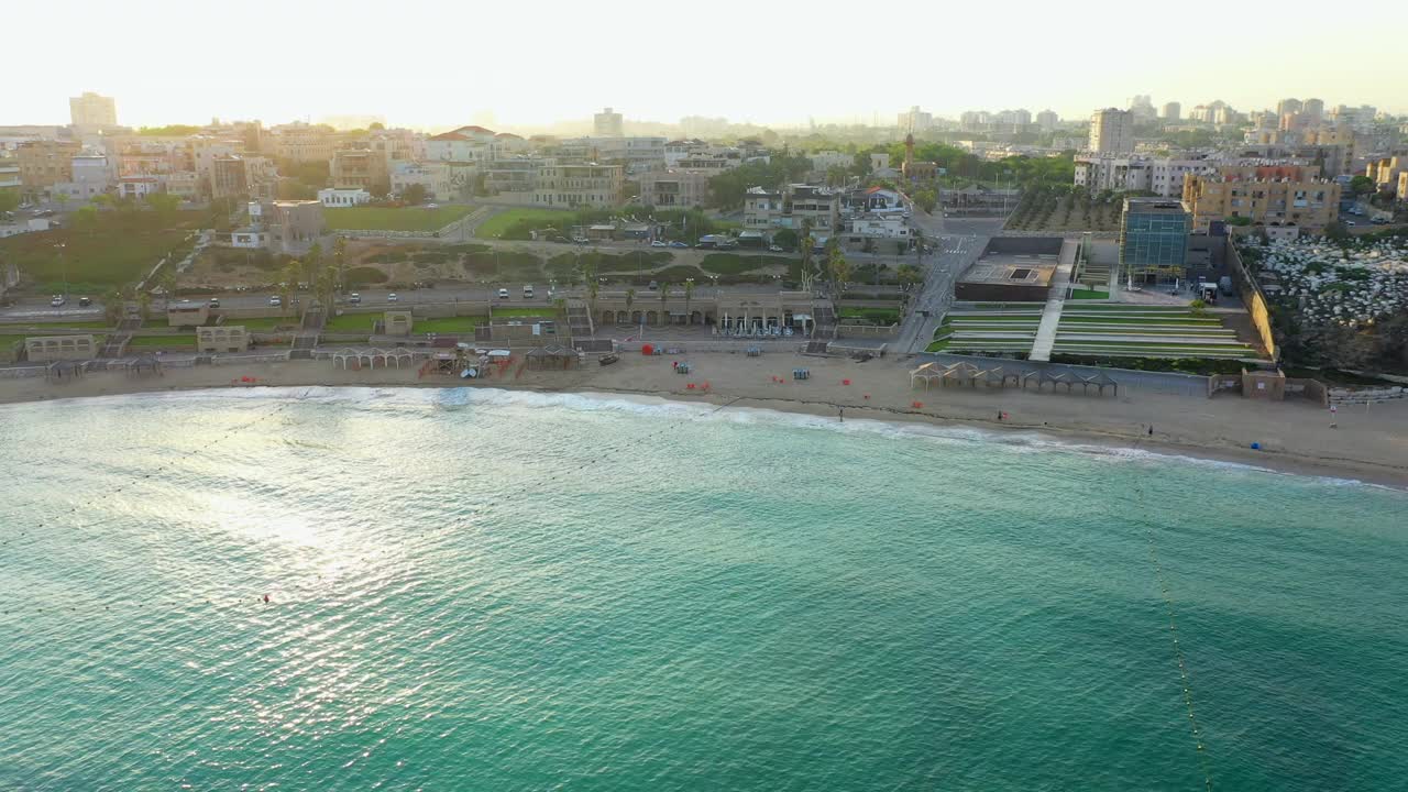 空中拍摄的海岸城市在日落，无人机从海滩向后上升-雅法，以色列视频素材