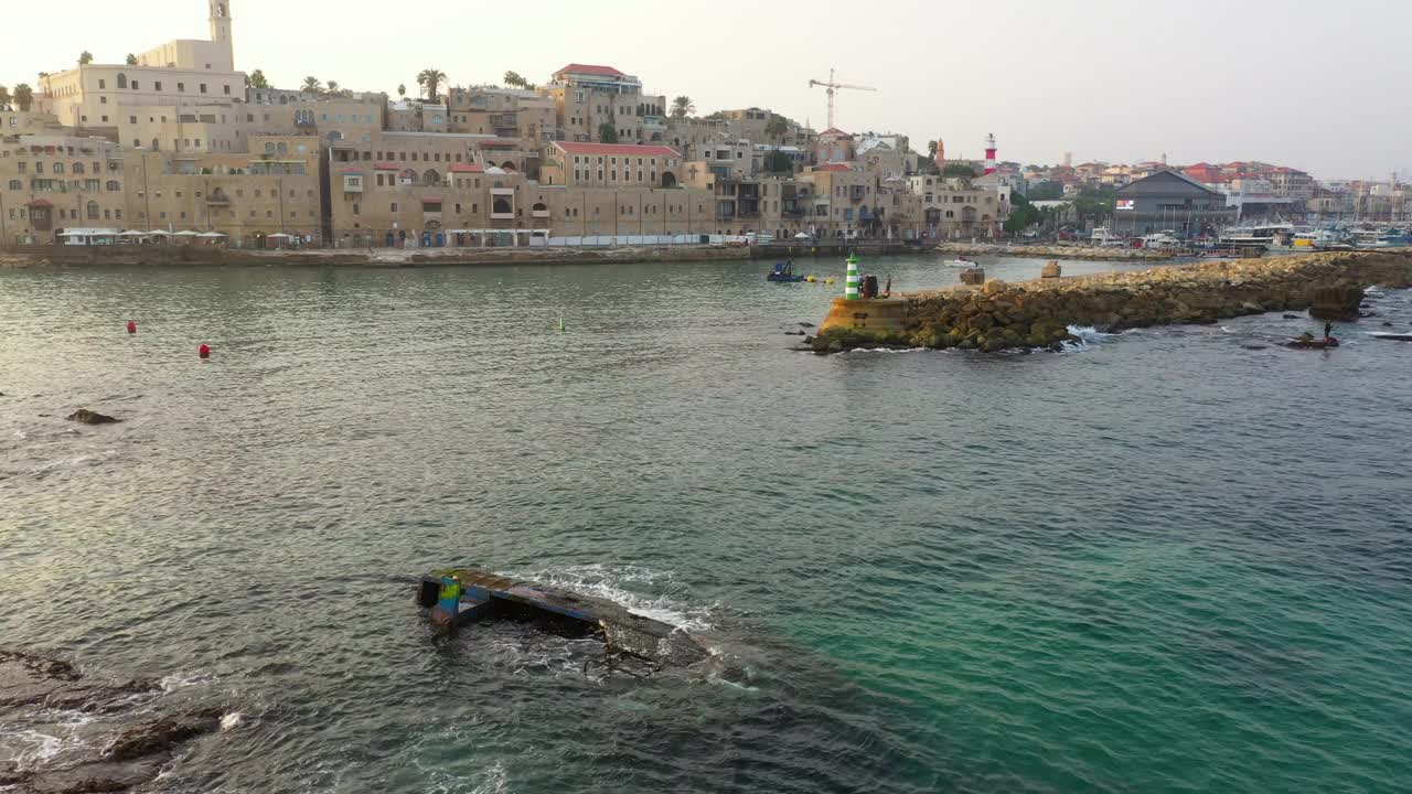 日落时分，无人机在建筑物附近的海岸线上空飞行，对城市和港口进行空中封锁拍摄——以色列雅法视频素材