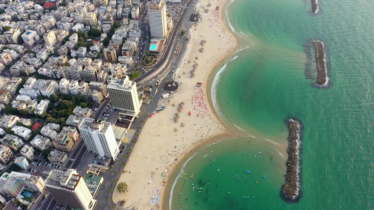 空中倾斜拍摄的人们在海滩上与Groynes在现代城市，无人机飞越城市景观-特拉维夫，以色列视频素材