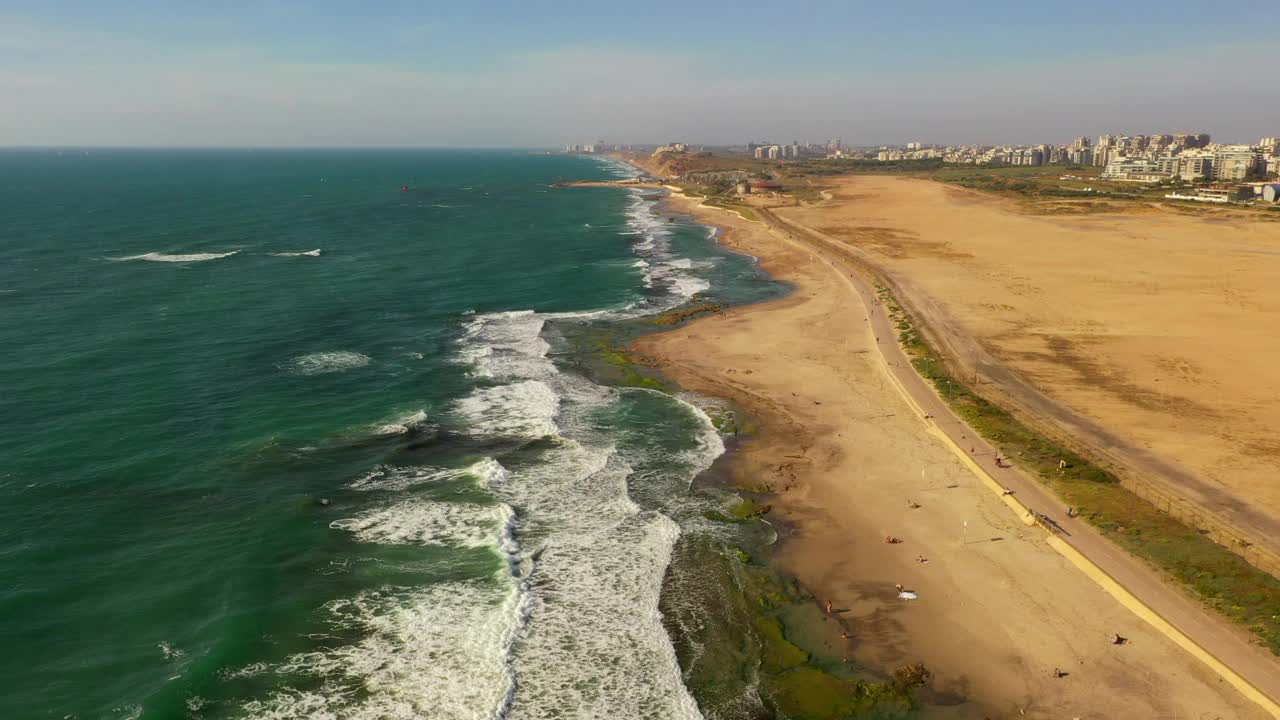 空中拍摄的海浪拍打在海滩上的天空，无人驾驶飞机向前飞在人们在城市的公园在阳光明媚的一天-特拉维夫，以色列视频素材