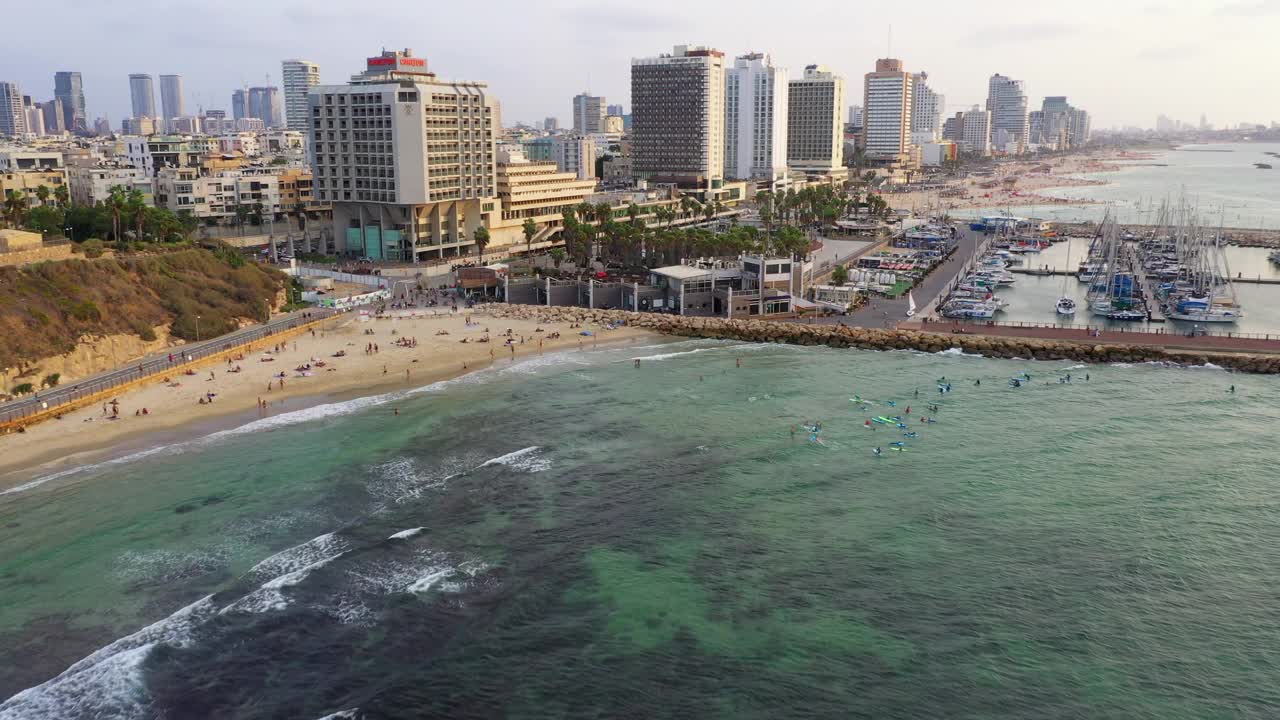 空中拍摄的海滩上的人在城市的酒店对天空，无人机下降在港口-特拉维夫，以色列视频素材