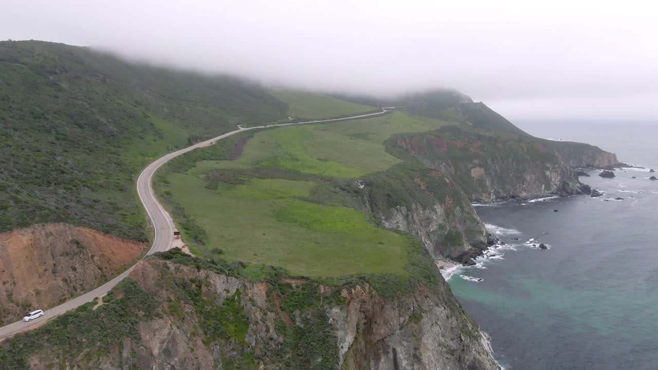 空中拍摄的车辆在著名的比克斯比溪桥上的悬崖，无人机向后飞从山下的雾-大苏尔，加利福尼亚视频素材