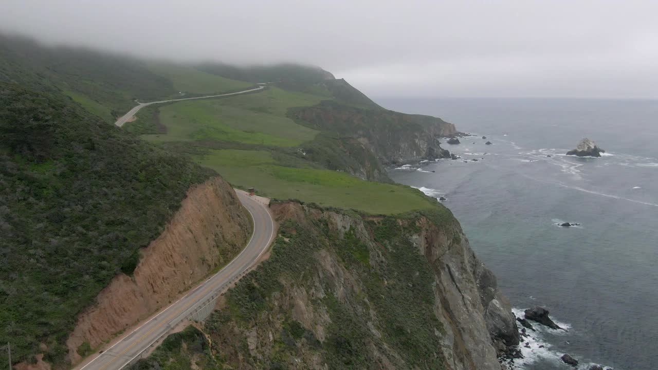 海浪溅在悬崖附近的道路上的车辆，无人机在雾天气期间向前飞过海岸线-大苏尔，加利福尼亚视频素材