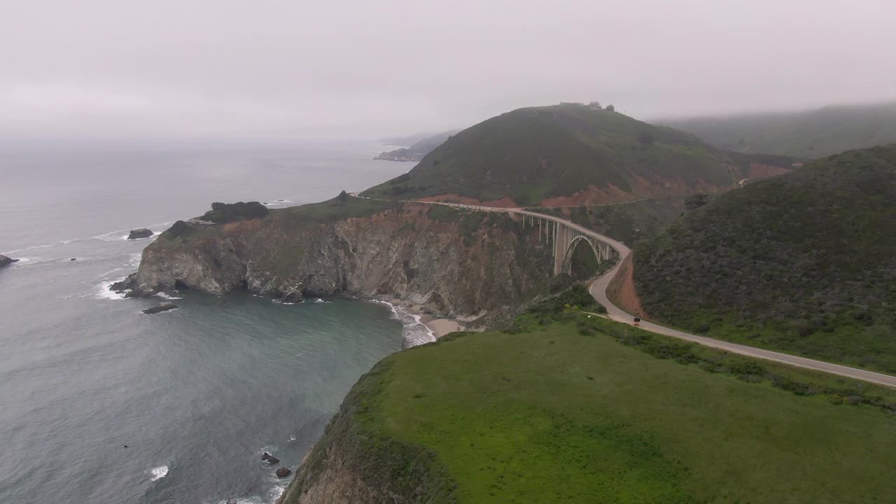 空中拍摄的汽车在受欢迎的比克斯比溪桥上的悬崖，无人机飞向山脉在雾下的海上-大苏尔，加利福尼亚视频素材