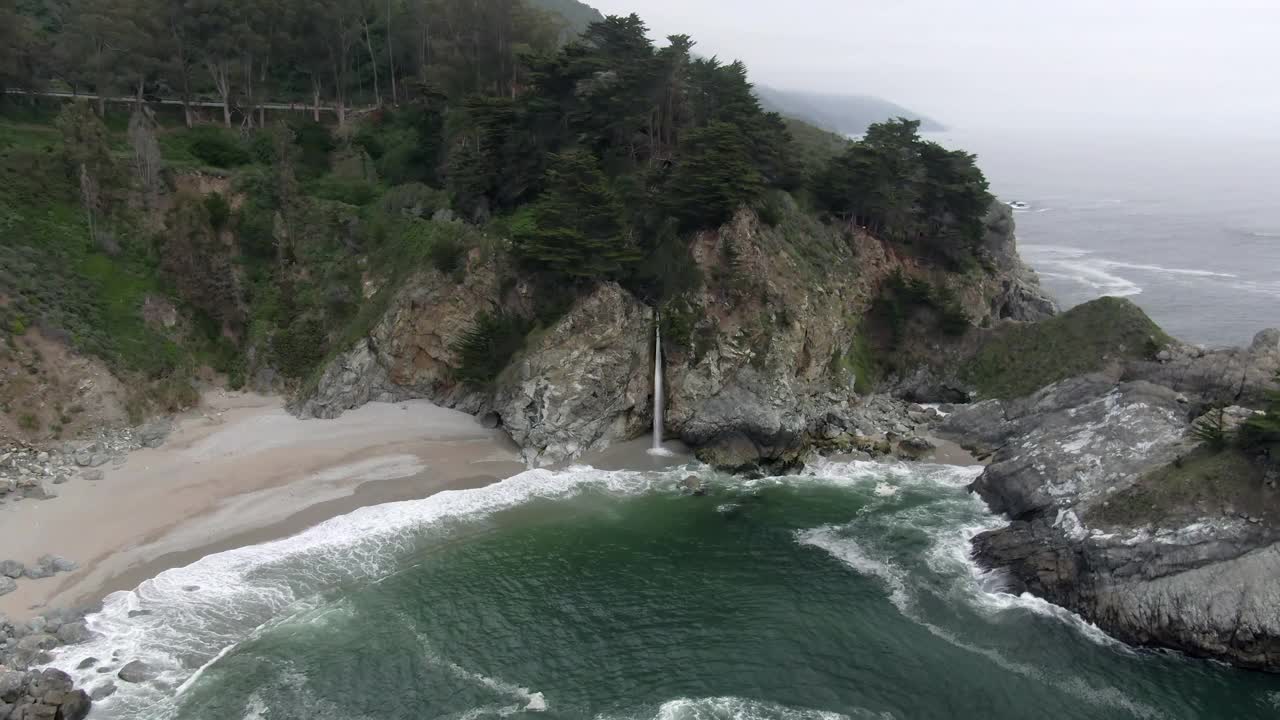 航拍美丽的麦克威瀑布从岩石悬崖在海滩，无人机飞向前拍打海岸-大苏尔，加利福尼亚视频素材