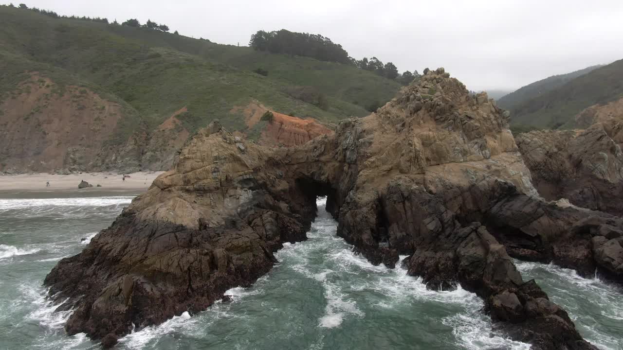 空中倾斜向下拍摄的浪花溅在锁眼拱门，无人机向前飞向人们在著名的Pfeiffer海滩-大苏尔，加利福尼亚视频素材