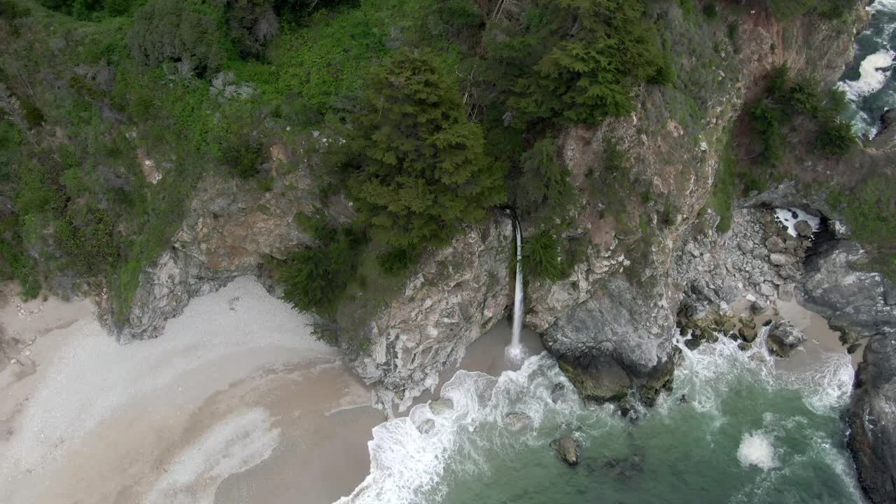 高空倾斜拍摄的麦克威瀑布从岩石悬崖在海滩，无人机向后飞行在海浪拍打海岸-大苏尔，加利福尼亚视频素材