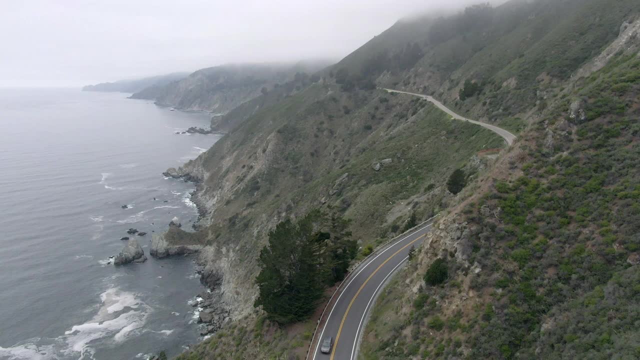 空中封锁拍摄的车辆在蜿蜒的沿海道路上越过山脉，无人机在海岸线上对着天空飞行-大苏尔，加利福尼亚视频素材