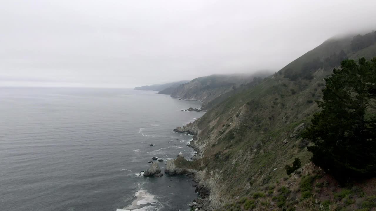 空中倾斜向下拍摄的海浪溅在海岸线上的天空，无人机向前飞行的山与海岸公路-大苏尔，加利福尼亚视频素材