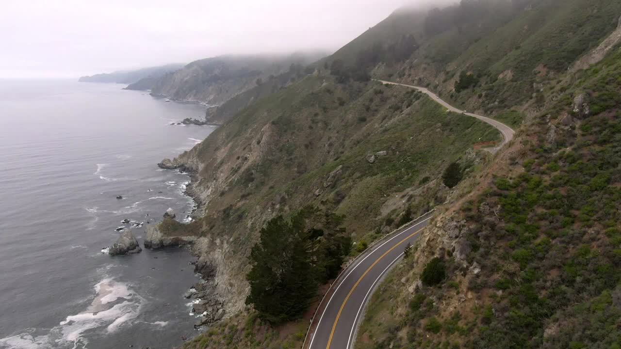 空中拍摄的车辆在蜿蜒的沿海道路上的山，无人机向前飞行的海岸线对天空-大苏尔，加利福尼亚视频素材