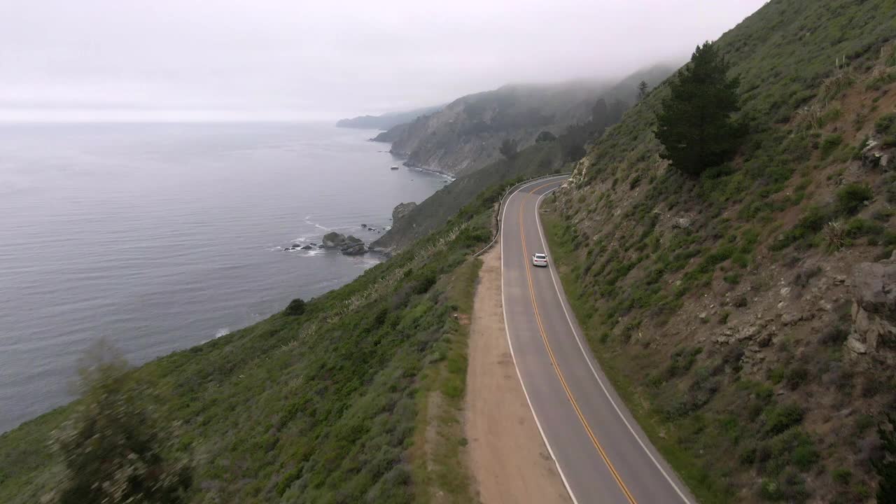 空中平移拍摄的车辆在海上蜿蜒的沿海道路上，无人机向前飞行的山脉对天空-大苏尔，加利福尼亚视频素材