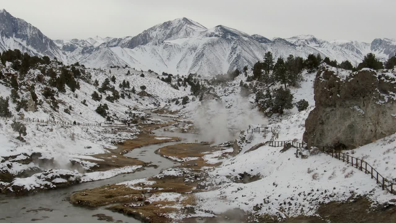 航拍的游客在小溪与蒸汽在雪中，无人机下降向前在热溪地质地点附近积雪覆盖的山脉-猛犸湖，加利福尼亚视频素材