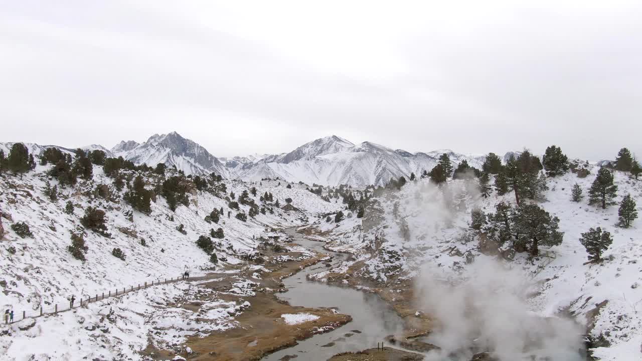 空中放大拍摄的蒸汽越过小溪在雪山中，无人机向后飞行在炎热的小溪地质地点在冬天-猛犸象湖，加利福尼亚视频素材