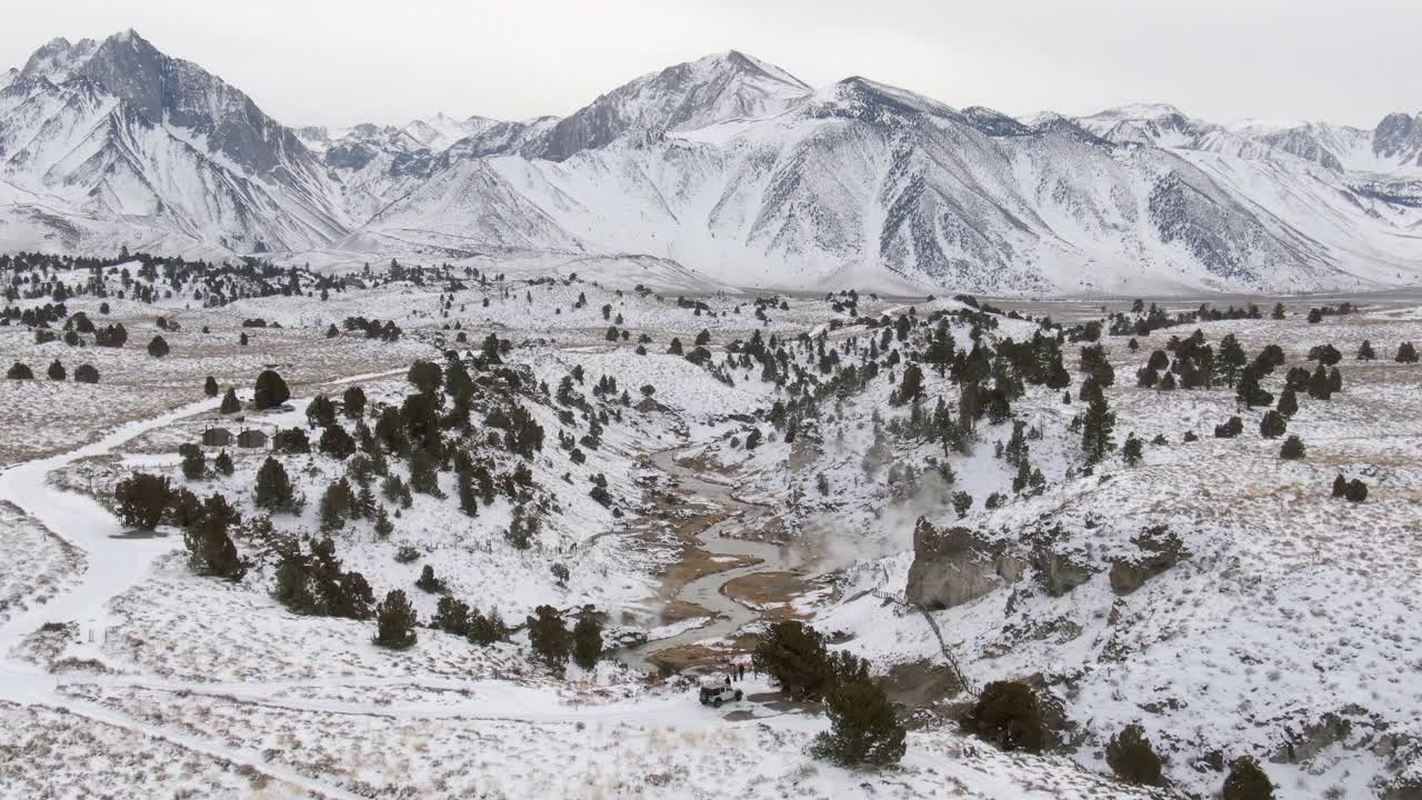 空中拍摄的热溪地质地点在雪中，无人机下降前向游客徒步在附近的雪峰山脉-猛犸湖，加利福尼亚视频素材