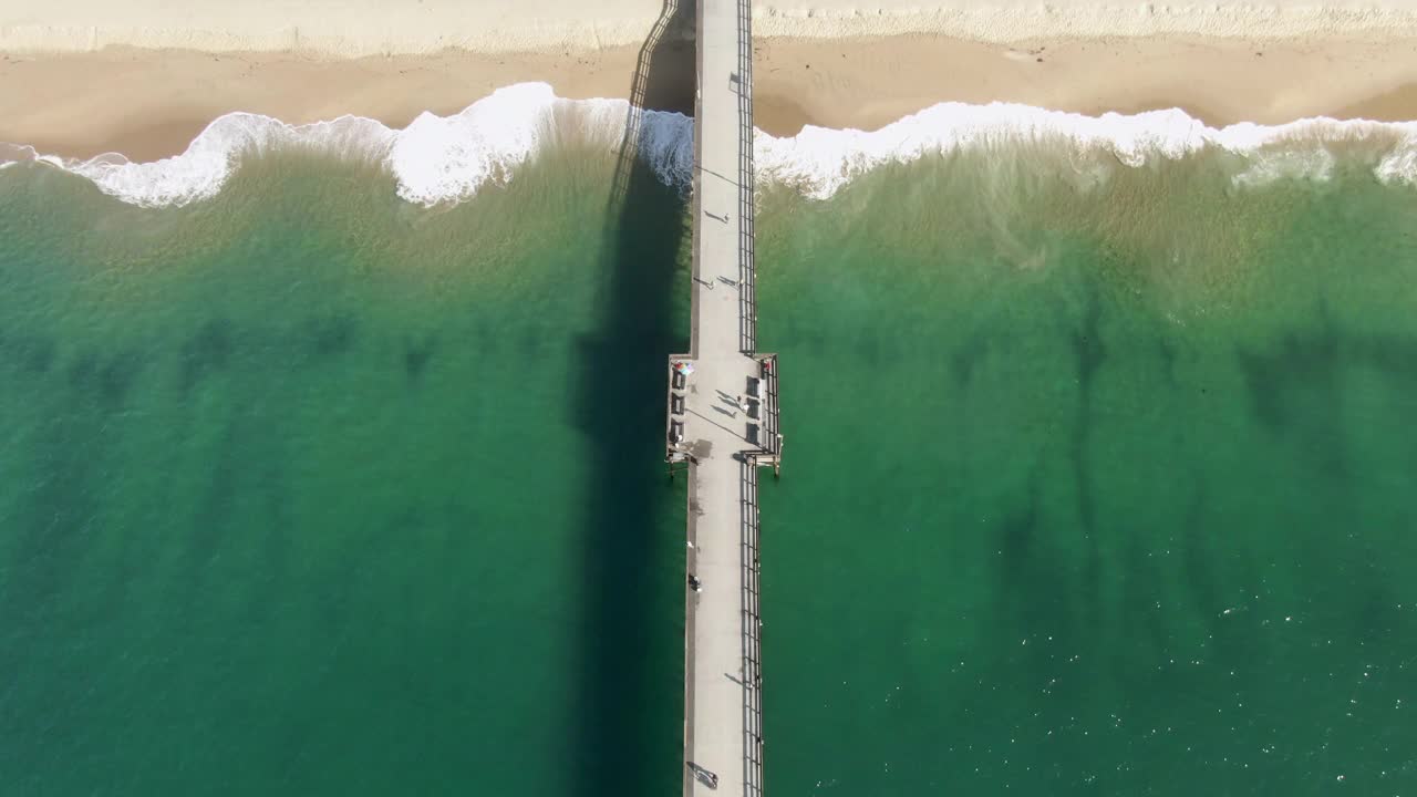 空中倾斜拍摄的人在Balboa码头溅起的波浪，无人机向后飞行在城市的海滩对天空在阳光日-新港海滩，加州视频素材