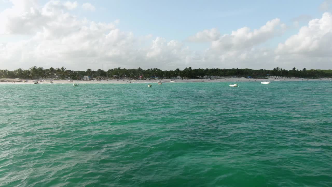 航拍海上的船与人们在海滩上享受，无人机向前飞向海岸对着天空在晴天-图卢姆，墨西哥视频素材