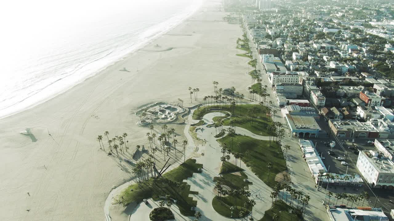 空中倾斜向下拍摄的人在海滩与威尼斯溜冰公园，无人机向前飞行在城市著名的地标-洛杉矶，加利福尼亚视频素材