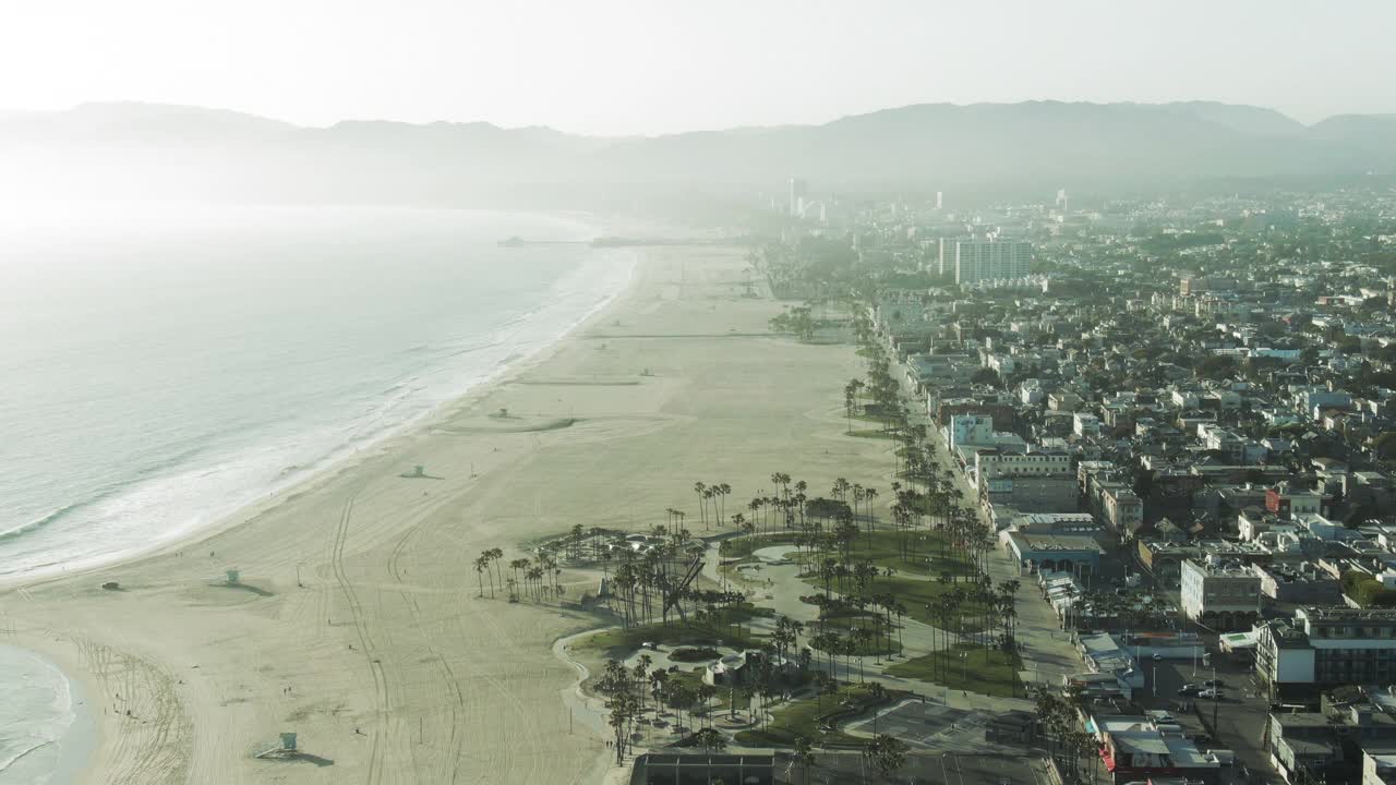 航拍的城市与威尼斯滑板公园在海滩上对着天空，无人机向后飞行在阳光明媚的一天建筑-洛杉矶，加利福尼亚视频素材