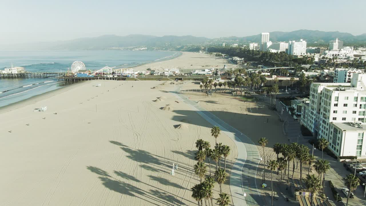 航拍海岸线上的著名码头在晴朗的天空下，无人机向后飞行在城市的海滩在早上-圣塔莫尼卡，加利福尼亚视频素材