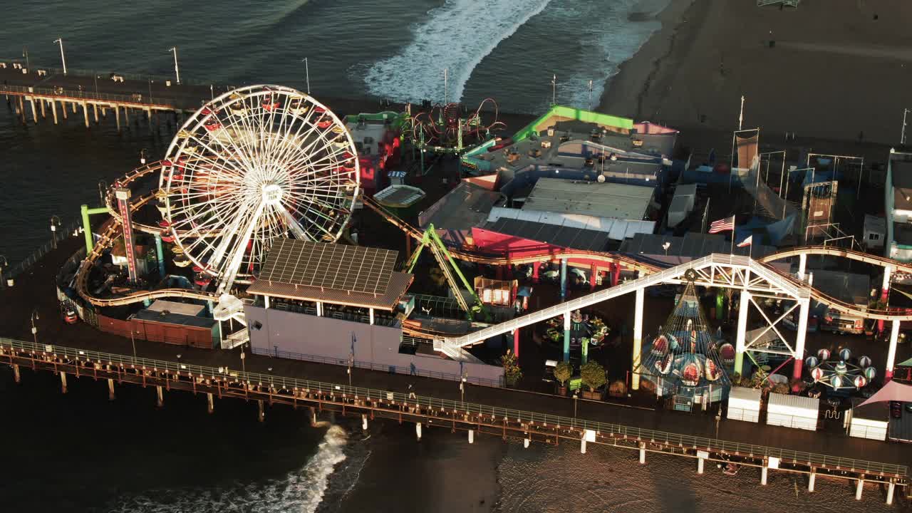 空中倾斜向上拍摄的著名码头在海滩对山脉，无人机向后飞行在城市对天空在日落-圣塔莫尼卡，加利福尼亚视频素材