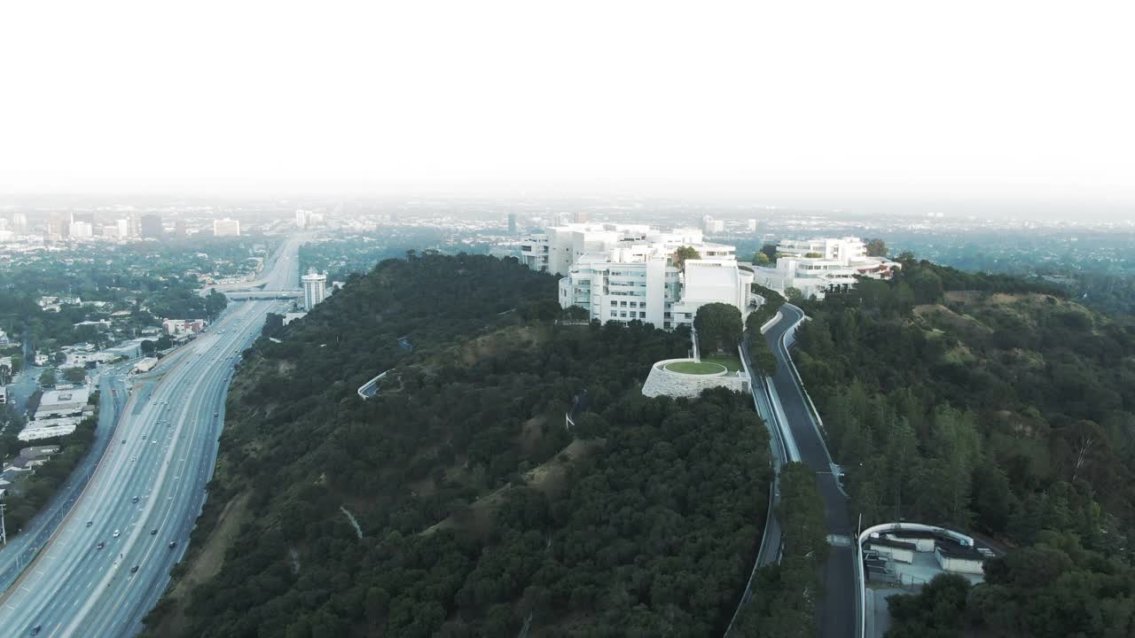 航拍著名的盖蒂中心在山上的城市景观，无人机飞向博物馆在日落天空的高速公路上的交通-洛杉矶，加利福尼亚视频素材