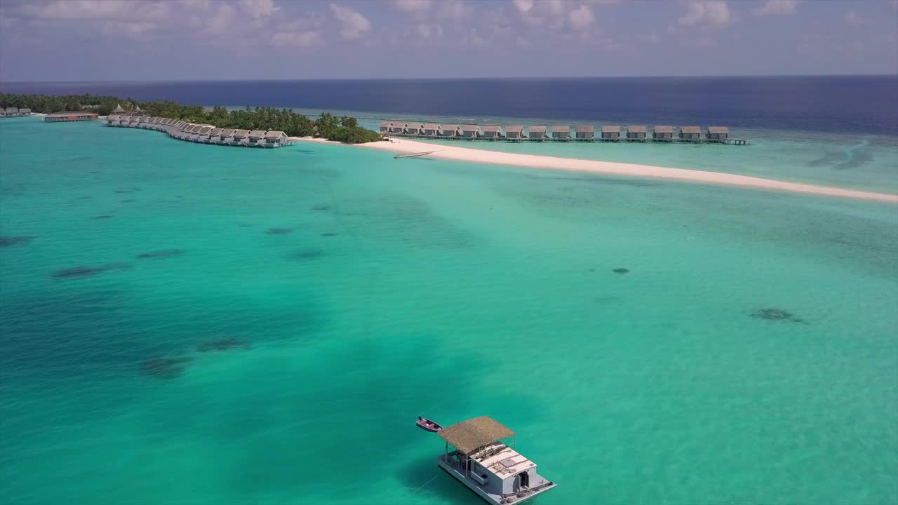 航拍拍摄的水平房在绿松石海对天空，无人机向前飞向豪华度假村在阳光明媚的一天-南马莱环礁，马尔代夫视频素材