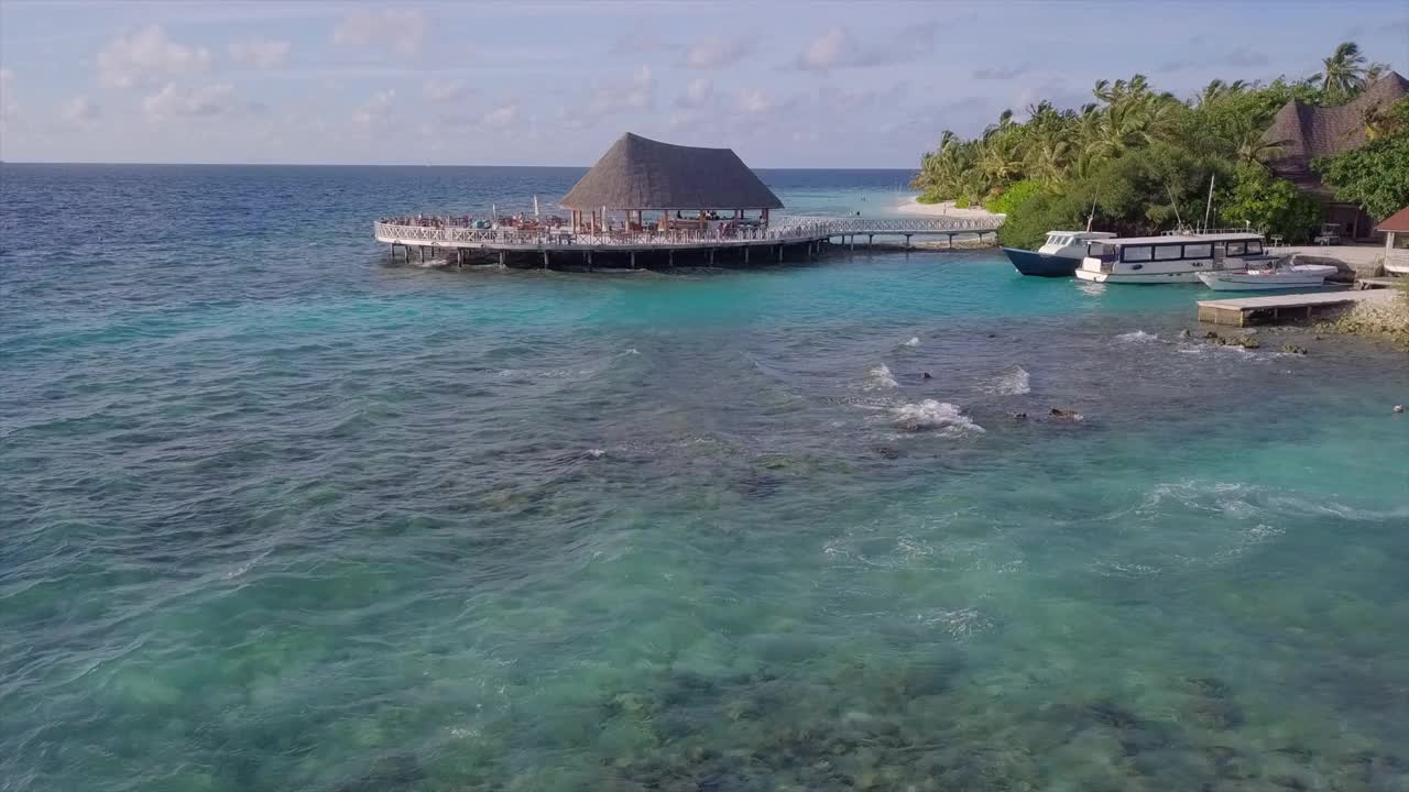 在马尔代夫南部马累环礁，海浪在海滩上溅起水花，无人机在餐厅附近飞行视频素材