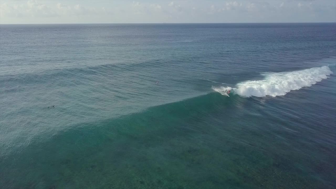 空中拍摄的人冲浪在海浪上对着天空，无人机向后飞溅水-南马累环礁，马尔代夫视频素材