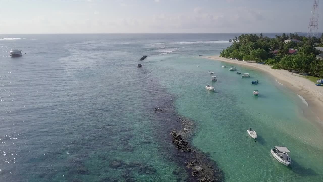 航拍停泊在海滩上的船对天空，无人机在晴朗的一天在绿松石海上向前飞行-南马累环礁，马尔代夫视频素材